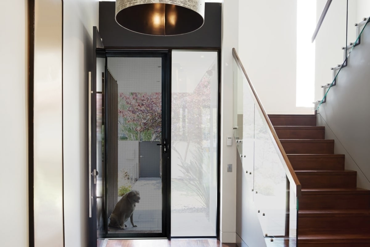 A contemporary house interior with a glass staircase and a Amplimesh PrivacyGuard security screen door at the front entrance.