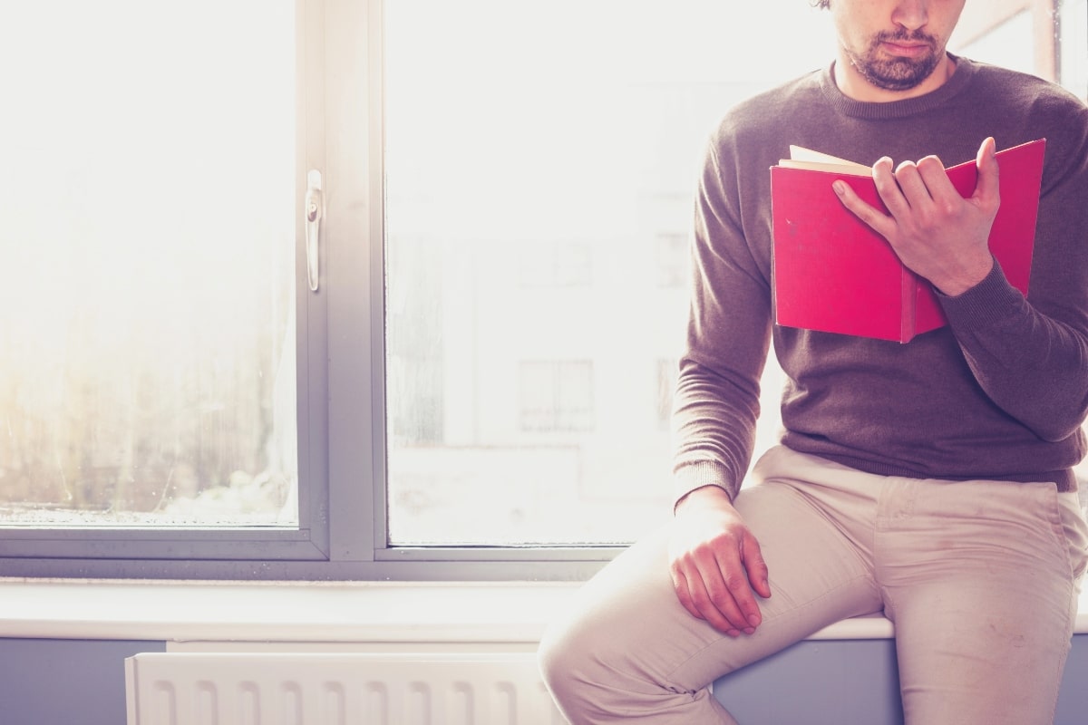 Natural light streaming through a window – A person sitting by a window reading a book, illustrating the effects of bright, direct sunlight and potential glare on indoor comfort.