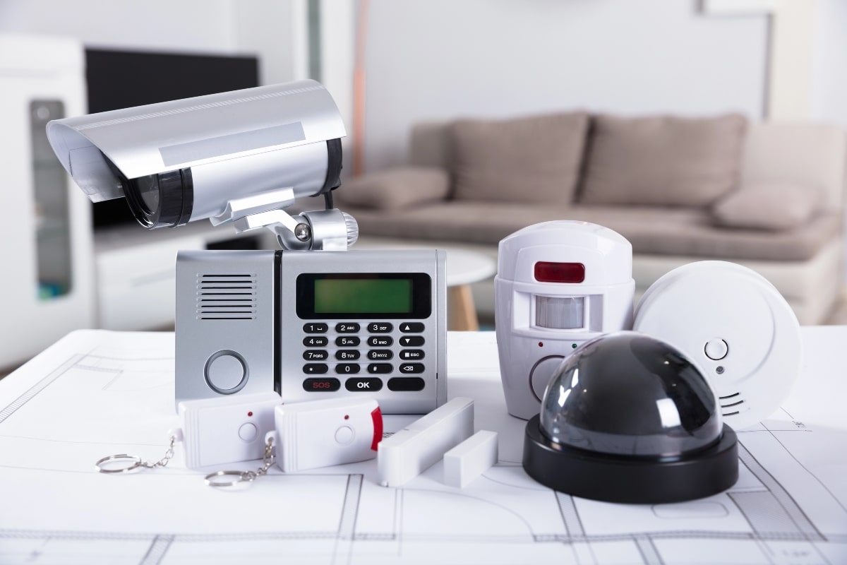 A set of home security equipment, including remote-controlled alarms, a smoke detector, and a keypad entry system, demonstrating key security measures for homeowners after relocating.