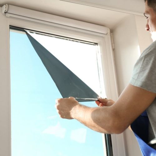 Applying window tinting for homes – A person carefully installing a dark window tint film on a glass window, ensuring a smooth application for privacy and UV protection.