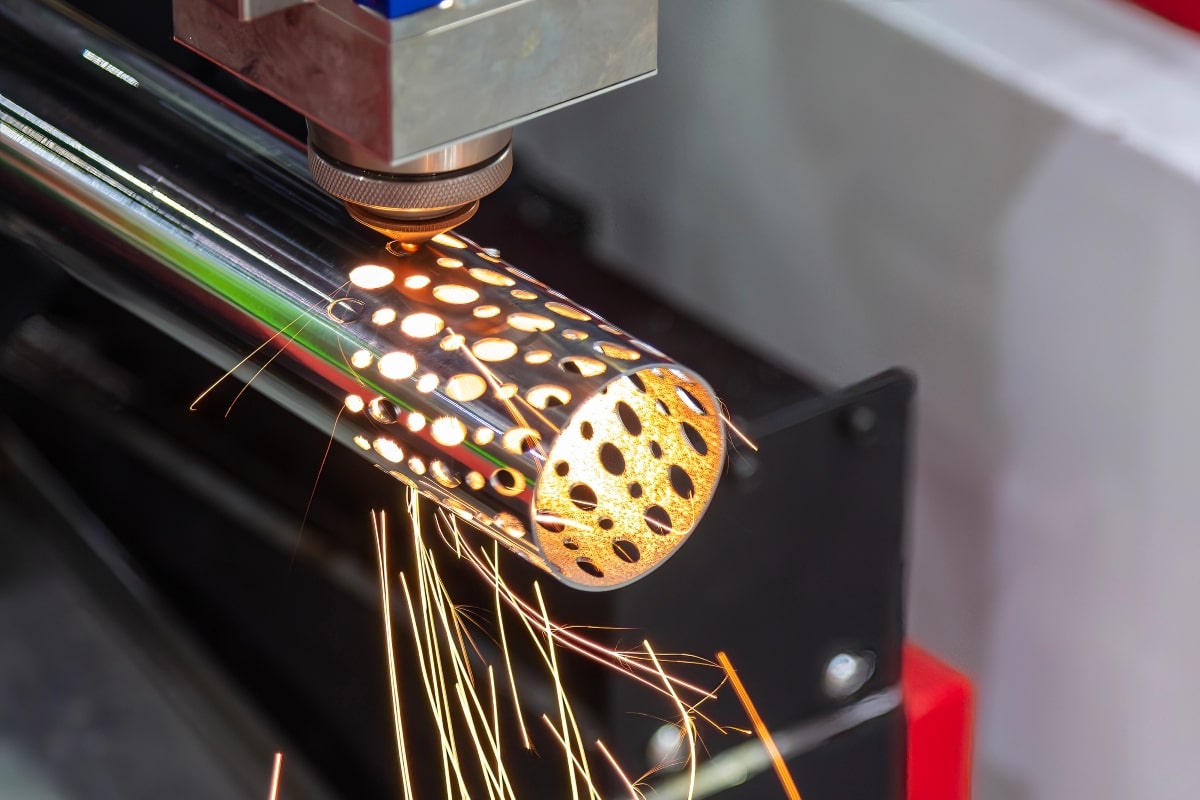 A laser cutting machine creating perforations on a steel tube, emitting sparks during the precise manufacturing process.