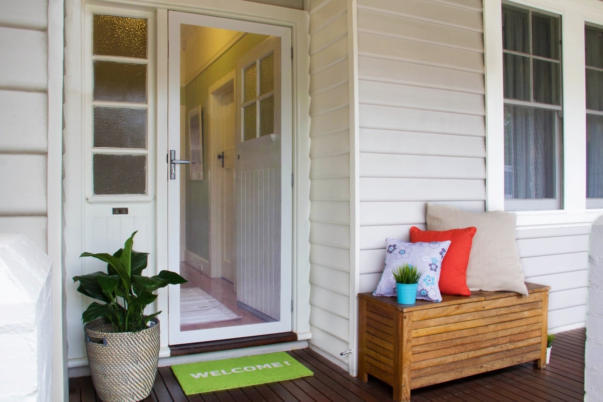 A charming home entrance featuring a secure white mesh door, potted plants, and a cosy seating area, reinforcing the importance of security upgrades when settling into a new house.